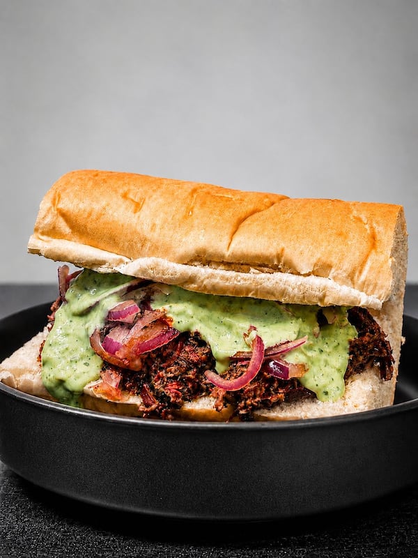 A fluffy white roll is filled with tandoori beef, pickled onions, and a sauce.