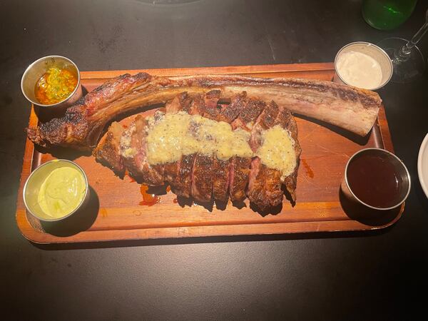 A sliced tomahawk steak served next to the bone on a wooden butcher's board.