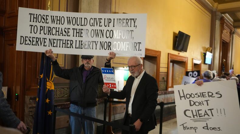 Protestors hold signs outside the Indiana Senate chamber before a vote to redistrict the state's congressional map at the Statehouse in Indianapolis, Thursday, Dec. 11, 2025. (AP Photo/Michael Conroy)