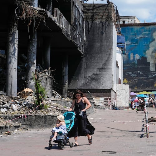 A mother pushes a stroller past a damaged building covered with street artist paintings and a big city marketplace that was destroyed recently by Russian missiles in Kyiv, Ukraine, Monday, June 22, 2026. (AP Photo/Efrem Lukatsky)