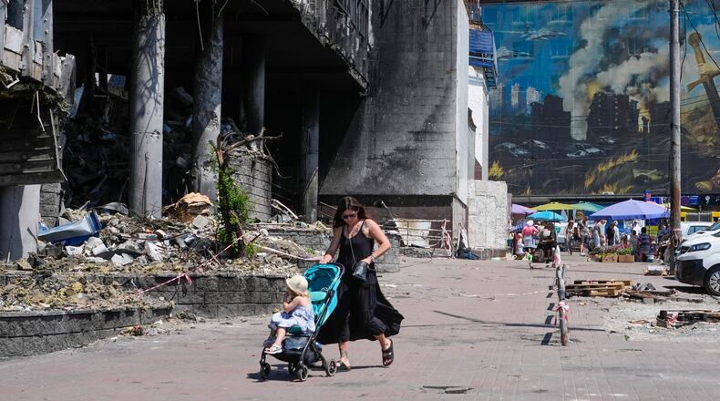 A mother pushes a stroller past a damaged building covered with street artist paintings and a big city marketplace that was destroyed recently by Russian missiles in Kyiv, Ukraine, Monday, June 22, 2026. (AP Photo/Efrem Lukatsky)
