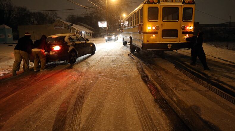 People work to push a stuck Atlanta school bus and a car on an icy stretch of University Avenue in Southwest Atlanta on Tuesday evening January 28, 2014. The bus was eventually moved off the road and left for the night.