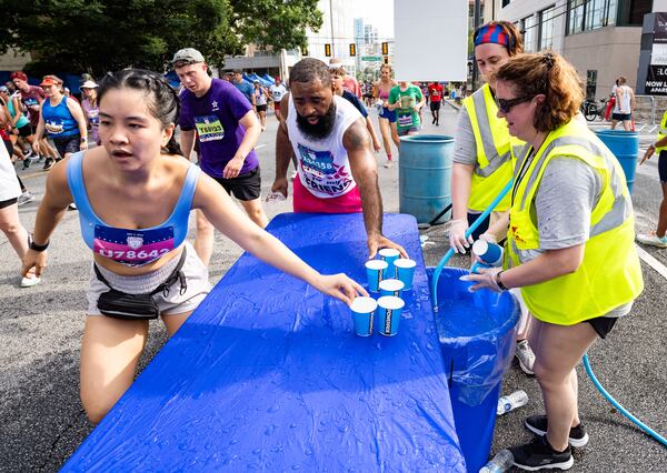 Atlanta Track Club volunteers fill cups of water for runners to take during the 55th running of the Atlanta Journal-Constitution Peachtree Road Race at "Cardiac Hill" on Peachtree Road NW in Atlanta on Thursday, July 4, 2024. (Seeger Gray/AJC)