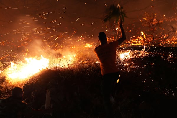 A man uses a branch to battle against a large wildfire burning in Kofinas, on the eastern Aegean island of Chios, Greece, late Sunday, June 22, 2025. (Pantelis Fykaris/Politischios.gr via AP)