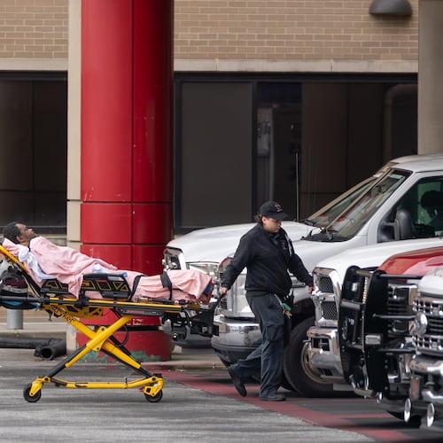 A medical crew wheels a patient across the parking area into Grady Memorial Hospital after parking across the street because the ambulance bay was full on Friday, May 1, 2026. (Ben Hendren for the AJC)