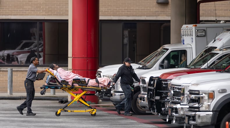A medical crew wheels a patient across the parking area into Grady Memorial Hospital after parking across the street because the ambulance bay was full on Friday, May 1, 2026. (Ben Hendren for the AJC)
