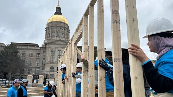 A line of volunteers holding a portion of wooden housing frame in front of the Georgia capitol.