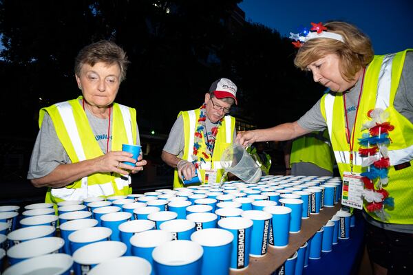 (From left) Atlanta Track Club volunteers Kristy and Vince Pinson of Marietta and Cathy Massett of Acworth lay out cups of water before the 55th running of the Atlanta Journal-Constitution Peachtree Road Race on Thursday, July 4, 2024. (Seeger Gray/AJC)