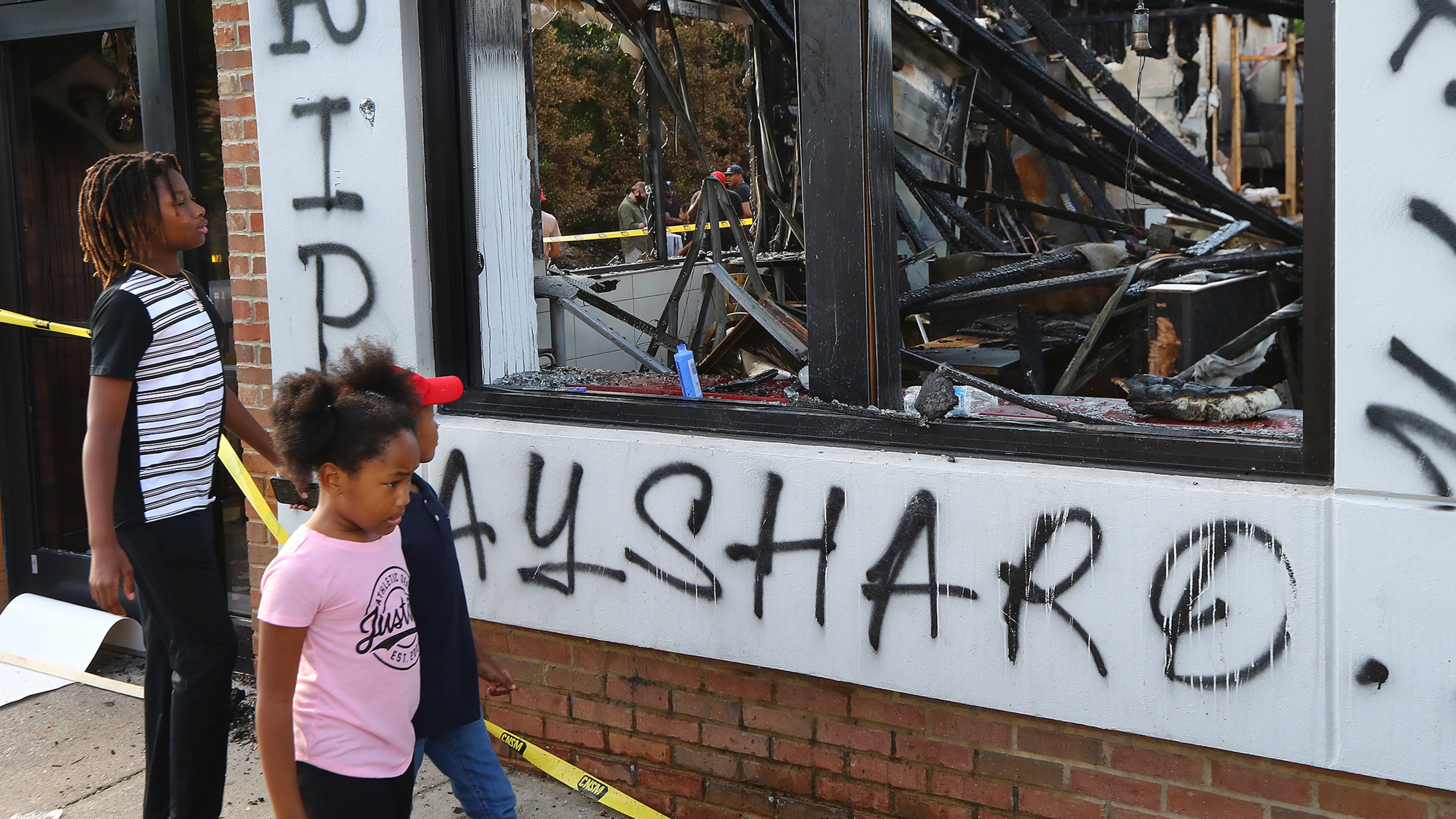 Children take in the burned-out Atlanta Wendy's where Rayshard Brooks, a 27-year-old Black man, was shot and killed by Atlanta police during a struggle in the drive-thru line on June 15, 2020. (Curtis Compton/AJC)