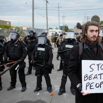 A demonstrator holds a sign reading "STOP BEATING PEOPLE" near a line of law enforcement as protesters gather outside an ICE processing facility in the Chicago suburb of Broadview, Ill., Saturday, Nov. 1, 2025. (AP Photo/Alex Brandon)