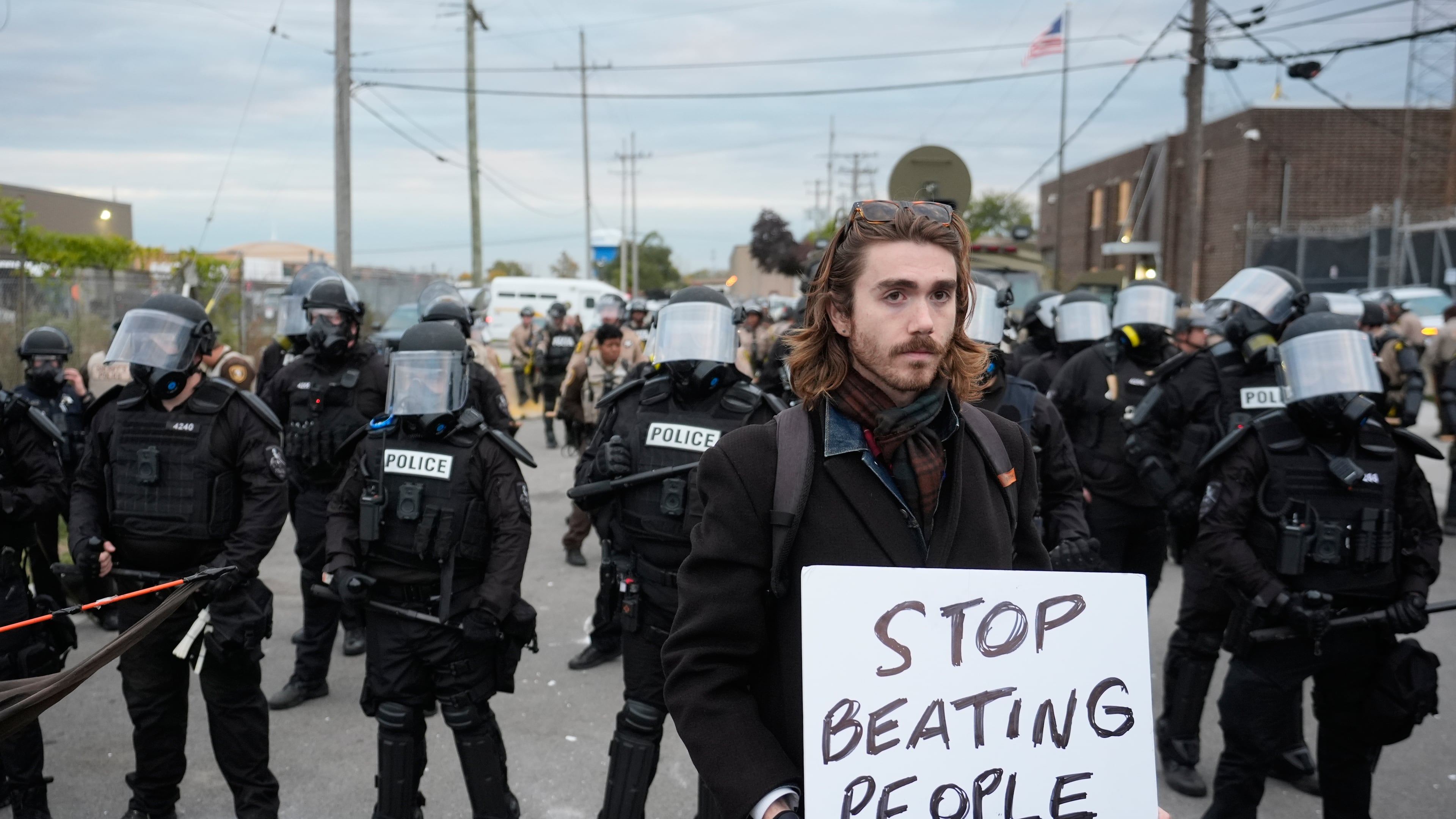 A demonstrator holds a sign reading "STOP BEATING PEOPLE" near a line of law enforcement as protesters gather outside an ICE processing facility in the Chicago suburb of Broadview, Ill., Saturday, Nov. 1, 2025. (AP Photo/Alex Brandon)
