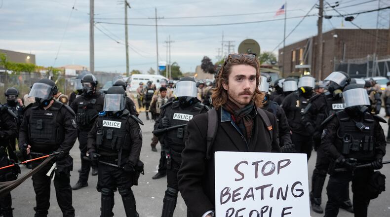 A demonstrator holds a sign reading "STOP BEATING PEOPLE" near a line of law enforcement as protesters gather outside an ICE processing facility in the Chicago suburb of Broadview, Ill., Saturday, Nov. 1, 2025. (AP Photo/Alex Brandon)