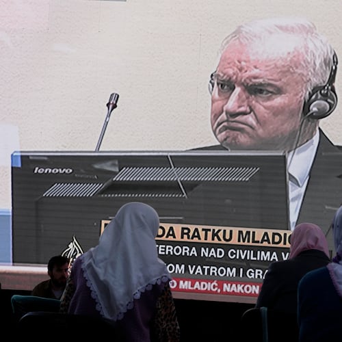 FILE - Women from Srebrenica watch a live broadcast from the Yugoslav War Crimes Tribunal in The Hague to learn the verdict for Bosnian Serb military chief Ratko Mladic, on the screen, at the memorial cemetery in Potocari near Srebrenica, eastern Bosnia, Tuesday, June 8, 2021.(AP Photo/Darko Bandic, File)