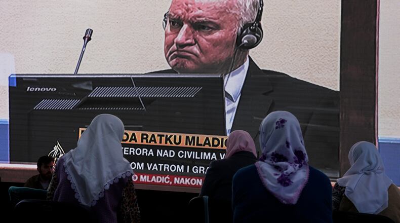 FILE - Women from Srebrenica watch a live broadcast from the Yugoslav War Crimes Tribunal in The Hague to learn the verdict for Bosnian Serb military chief Ratko Mladic, on the screen, at the memorial cemetery in Potocari near Srebrenica, eastern Bosnia, Tuesday, June 8, 2021.(AP Photo/Darko Bandic, File)