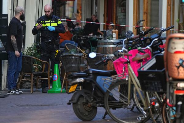 A police officer speaks to a man near a cordoned-off area after a stabbing near Dam Square in central Amsterdam, Thursday, March 27, 2025. (AP Photo/Peter Delong)