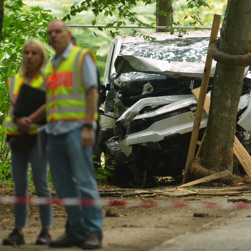 Police officers stand near a vehicle crashed into a tree after driving into a crowd near Berlin's annual Pride event, in Berlin, Germany, Sunday, July 26, 2026. (AP Photo/Markus Schreiber)