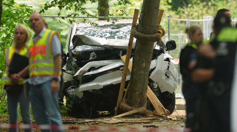Police officers stand near a vehicle crashed into a tree after driving into a crowd near Berlin's annual Pride event, in Berlin, Germany, Sunday, July 26, 2026. (AP Photo/Markus Schreiber)
