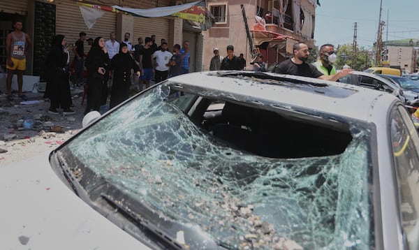 People gather next to a car that was damaged in an Israeli airstrike in Nabatieh town, south Lebanon, Friday, June 27, 2025. (AP Photo/Mohammed Zaatari)
