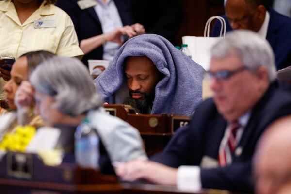 State Rep. El-Mahdi Holly, D-Stockbridge, huddles under a blanket on Sine Die, the last day of the legislative session. (Arvin Temkar/AJC)
