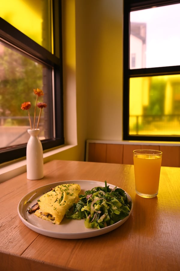 A restaurant table holds a plate with an omelet and a green salad, with a glass of orange juice to the right and a small vase of flowers to the left.