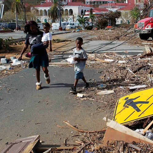 FILE - A woman and her children walk past debris left by Hurricane Irma in Charlotte Amalie, St. Thomas, U.S. Virgin Islands, on Sept. 10, 2017. (AP Photo/Ricardo Arduengo, File)