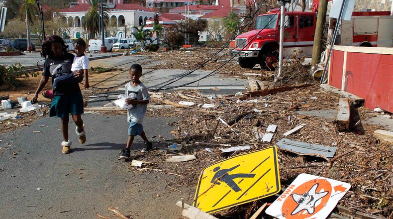 FILE - A woman and her children walk past debris left by Hurricane Irma in Charlotte Amalie, St. Thomas, U.S. Virgin Islands, on Sept. 10, 2017. (AP Photo/Ricardo Arduengo, File)
