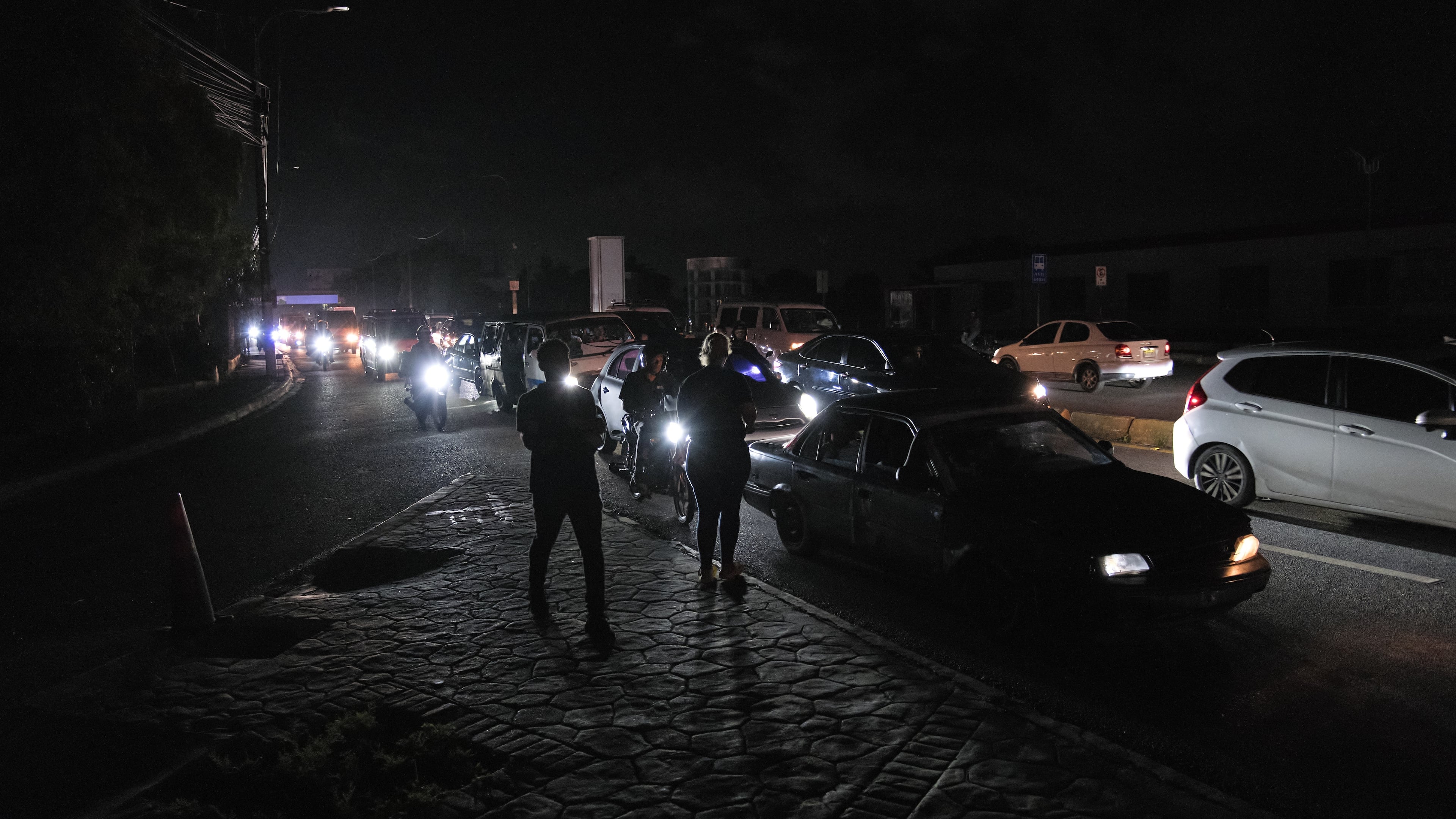 People watch as vehicles drive past during a blackout in Santo Domingo, Dominican Republic, Tuesday, Nov. 11, 2025. (AP Photo/Ricardo Hernandez)