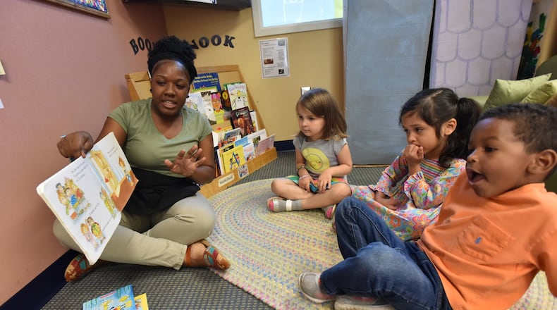 Ashton Aiken reads a book to (from left) Liliana Woods, 4, Carmen Castro, 3 and Eric Revell, 3, at Sheltering Arms International Village Center in 2018. HYOSUB SHIN / HSHIN@AJC.COM