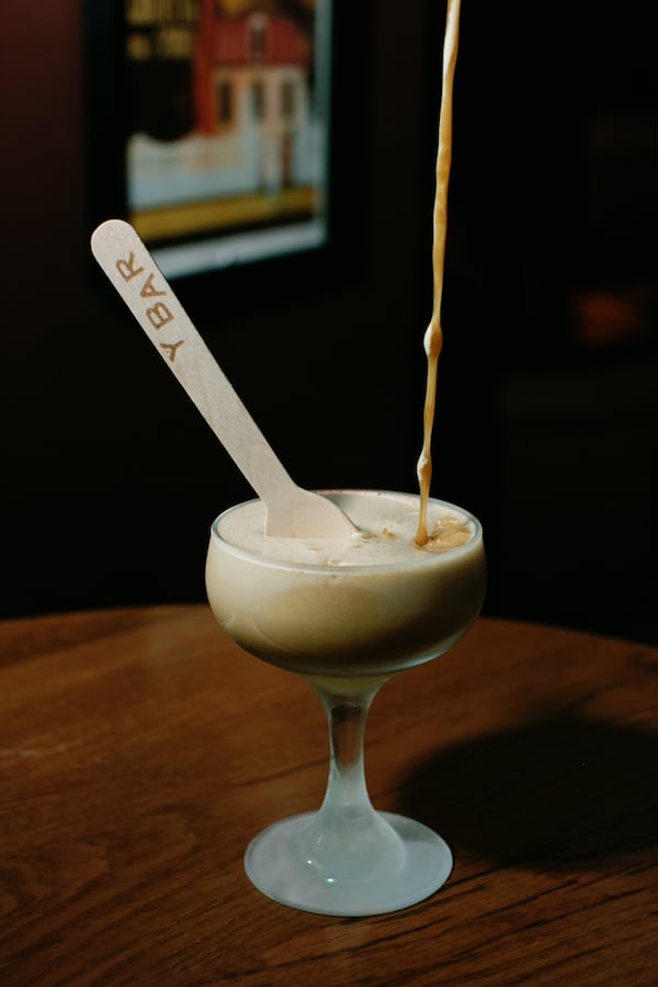 Y Bar's take on an espresso martini sits in a coup glass on a wooden table with a wooden spoon sticking out of it.