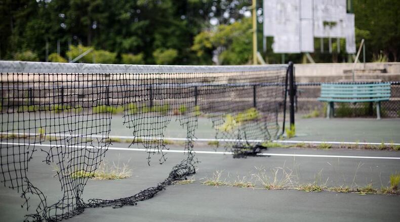 In this July 19, 2016, photo, the derelict netting and scoreboard in the background on a tennis court stand at the Stone Mountain Tennis Center, home of the 1996 Summer Olympic Games tennis events, in Stone Mountain, Ga. The permanent tennis facility built in a corner of Stone Mountain Park quickly became a money loser and now sits idle, weeds growing through the outer courts and the scoreboard in disrepair. (AP Photo/David Goldman)