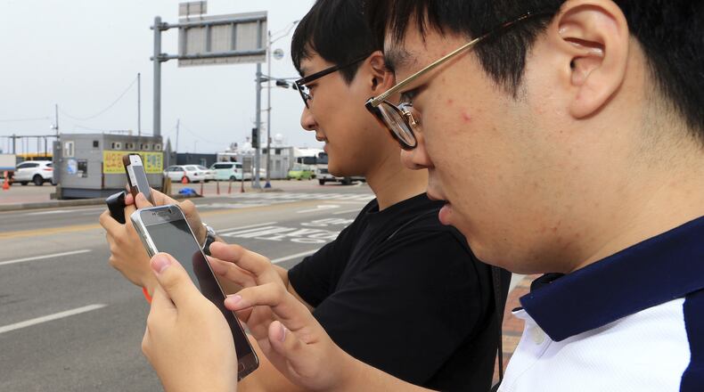 In this July 13, 2016 photo, two South Koreans play the Pokemon Go game with their mobile phones in Sokcho, South Korea. The seaside South Korean city of Sokcho is enjoying a surge of visitors who are wandering the streets at all hours as they look at their smartphones. It appears to be the only place in the country where Pokemon Go players can chase the mobile game’s virtual monsters. (Lee Jong-hun/Yonhap via AP)