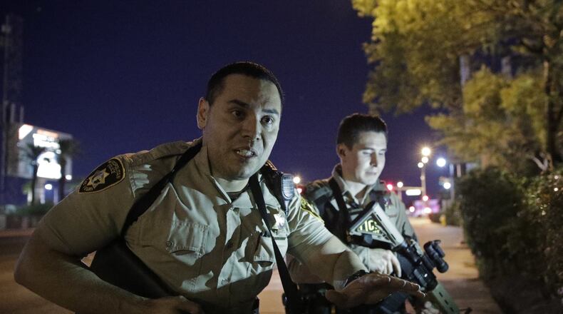 Police officers advise people to take cover near the scene of a shooting near the Mandalay Bay resort and casino on the Las Vegas Strip, Sunday night in Las Vegas. (AP Photo/John Locher)
