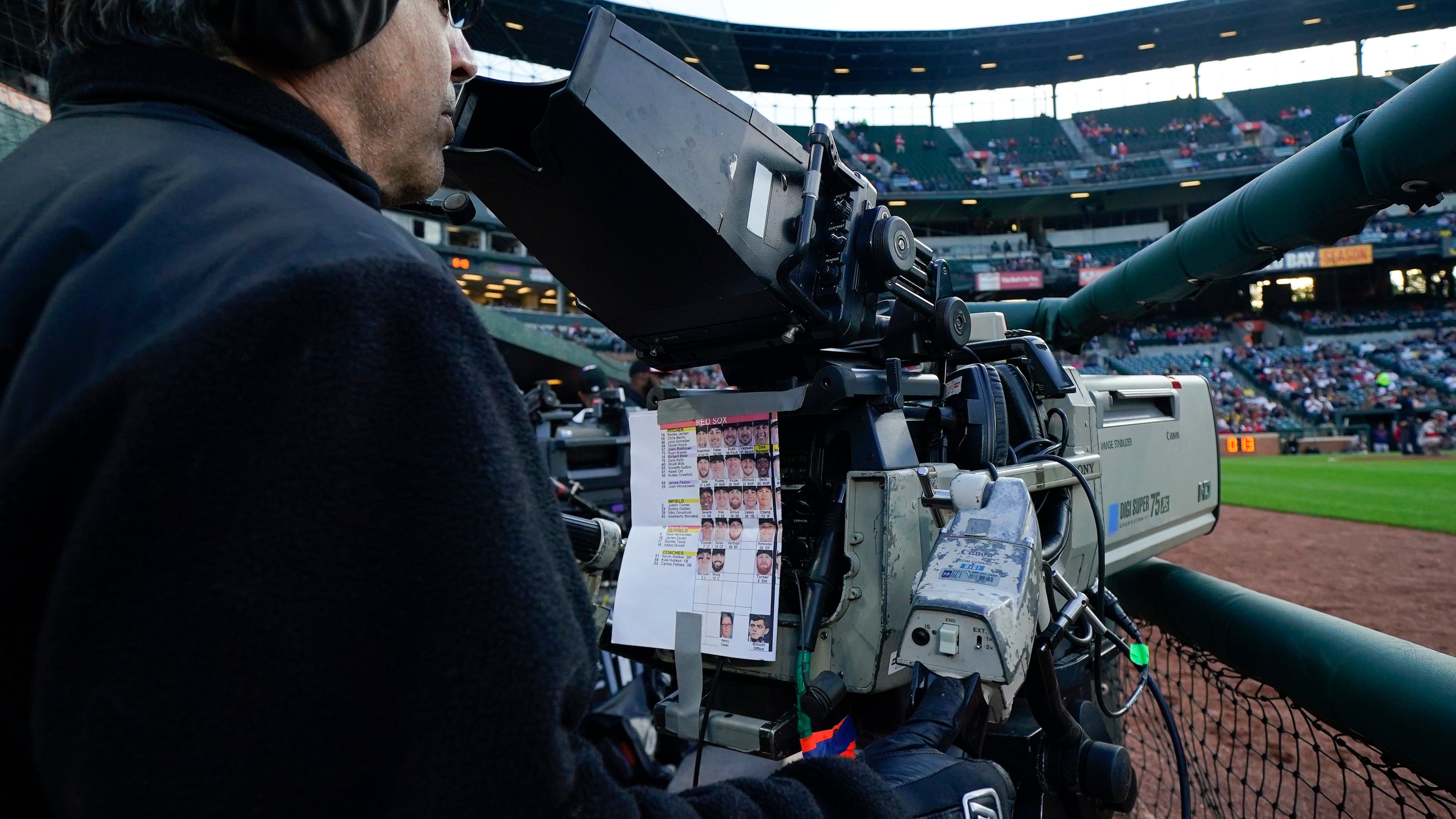 FILE - A sheet showing Boston Red Sox players photos hangs from a camera as a broadcast operator works during the first inning of a baseball game between the Baltimore Orioles and the Red Sox, Monday, April 24, 2023, in Baltimore, Md. (AP Photo/Julio Cortez, File)