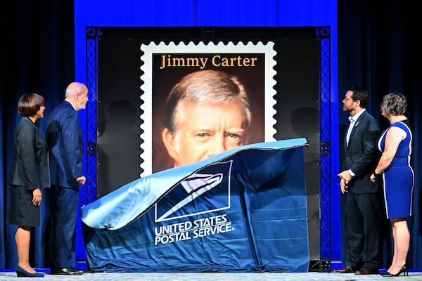 Crystal Edmonson, broadcast dditor of Atlanta Business Chronicle (from left); Thomas Marshall, general counsel of USPS; Jason Carter, grandson of former President Jimmy Carter; and Beth Davis, chief operating officer of the Carter Center, unveil the Jimmy Carter "forever" stamp in Atlanta on Wednesday. (Hyosub Shin/AJC)