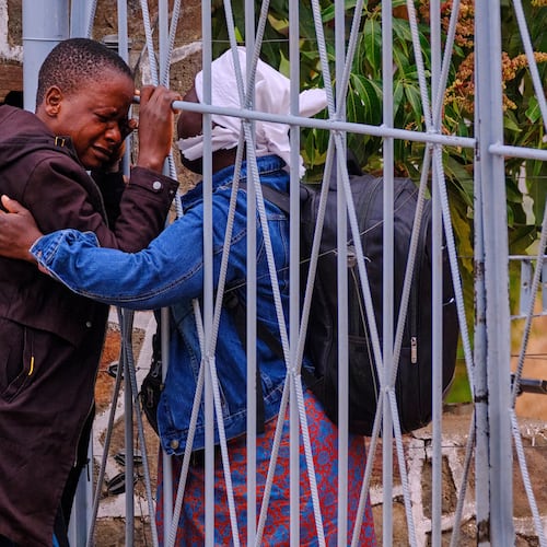 Philis Hamandise, center, is embraced through a gate by a colleague at a victim identification center after losing her 9-year-old daughter and 6-year-old nephew in a ferry capsizing on Lake Kariba, in Kariba, Zimbabwe, Thursday, Aug. 13, 2026. (AP Photo/Mkhululi Thobela)