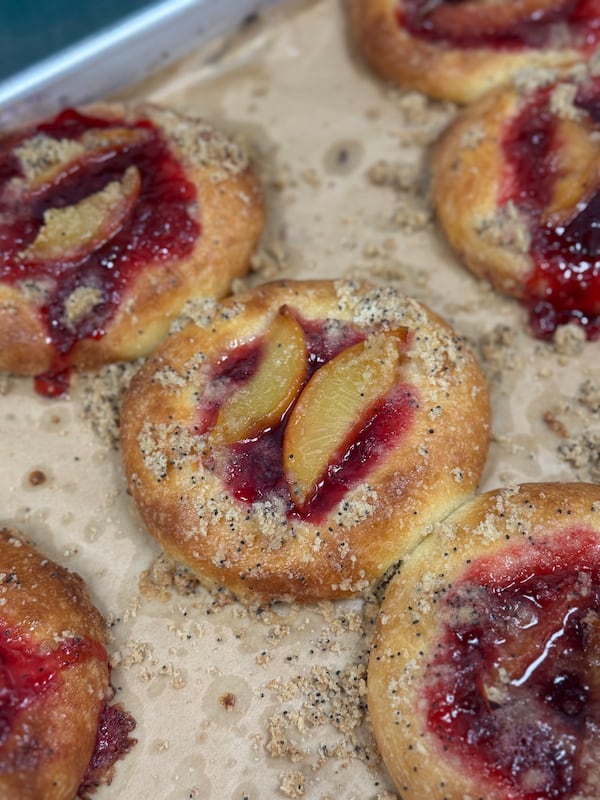 A tray full of brioche buns with a filling of baked peaches in the center of each.
