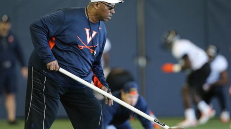 In this March 29, 2016 photo provided by the University of Virginia, assistant head coach Ruffin McNeill works with players during a team practice in Charlottesville, Va. McNeill no longer has the big corner office, and he says thay's fine with him. (Jim Daves/Univ. of Virginia via AP)