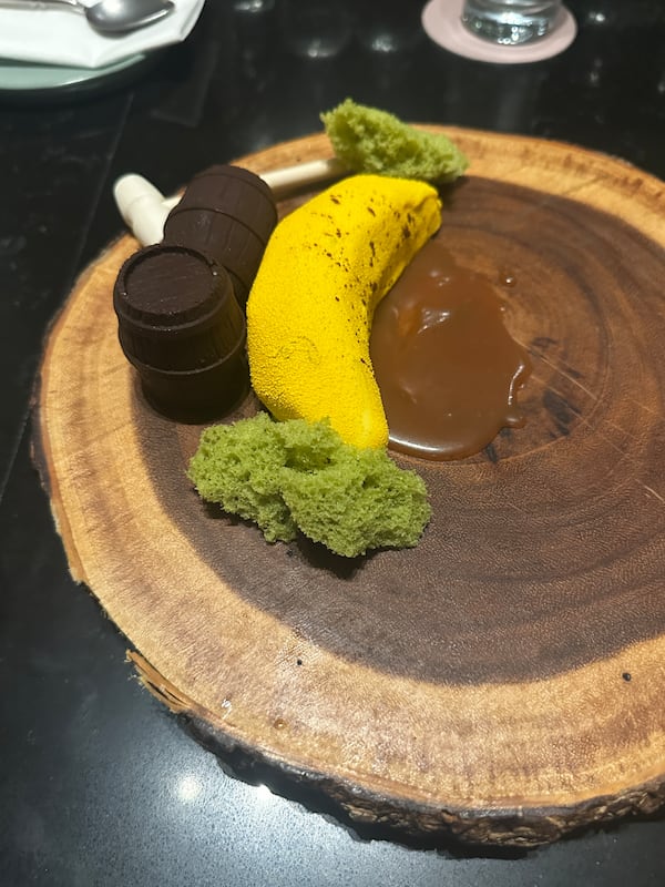 A trompe l'oeil banana dessert sits next to chocolate barrels making a Donkey Kong themed plate.