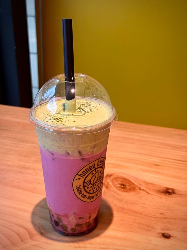 A purple and green boba drink in a plastic cup with a label that reads honey bubble.