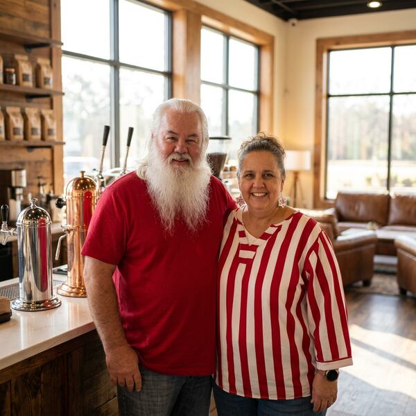 A large bearded man with white hair and beard stands next to a smaller woman with short hair and a striped shirt