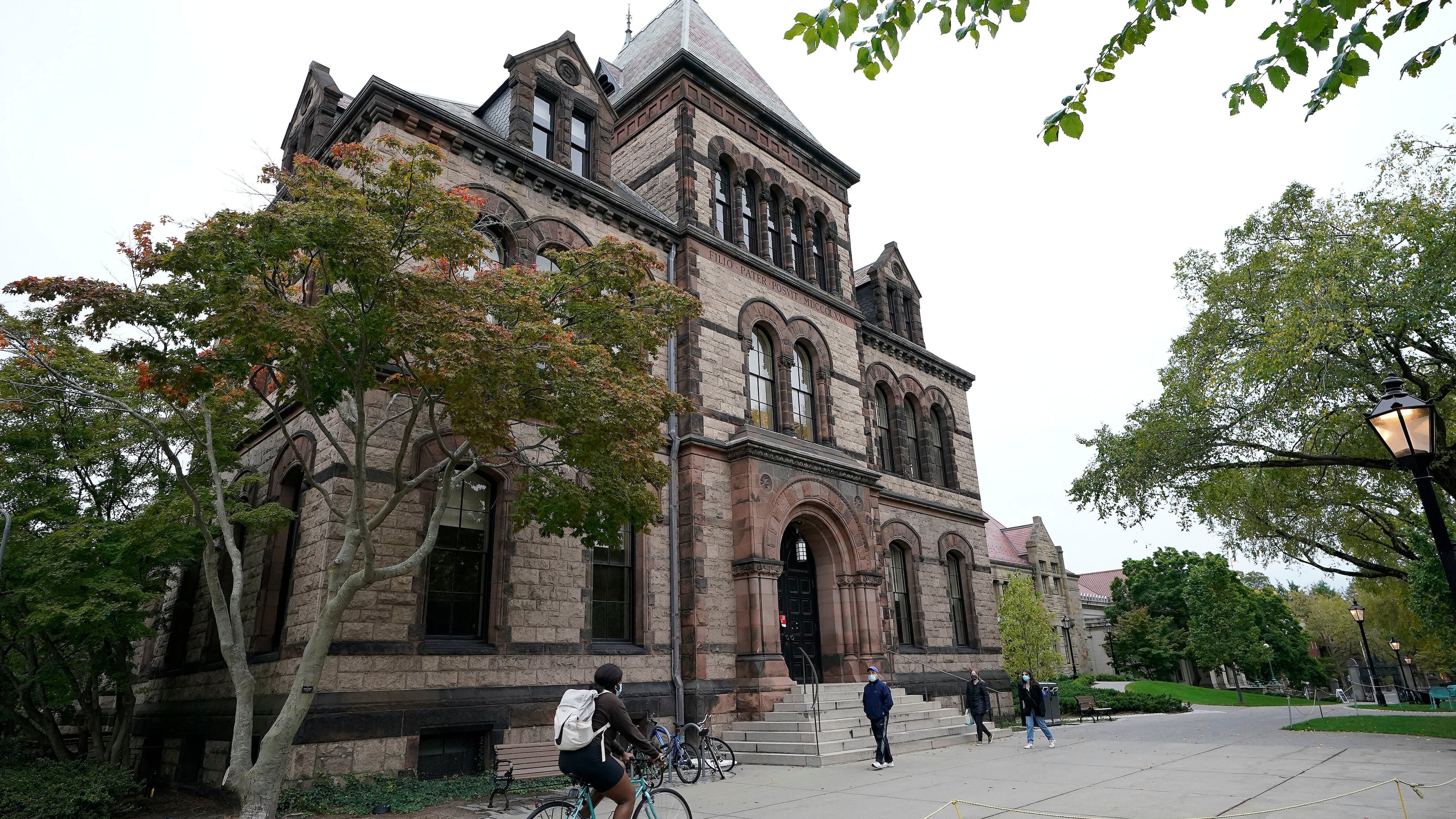 FILE - Passers-by walk and ride along a path on the campus of Brown University, in Providence, R.I., Monday, Oct. 12, 2020. (AP Photo/Steven Senne, File)