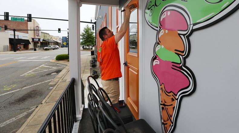 Brian Lambert paints a door as he gets ready to reopen Scoops, the ice cream shop he and his wife, Christie, own in Forsyth. They plan to take advantage of Gov. Brian Kemp’s order to allow some of the state’s businesses to reopen Friday after they have been shuttered in the midst of the coronavirus pandemic. “We have to open our doors, or our business will go under,” Christie Lambert said. Curtis Compton ccompton@ajc.com