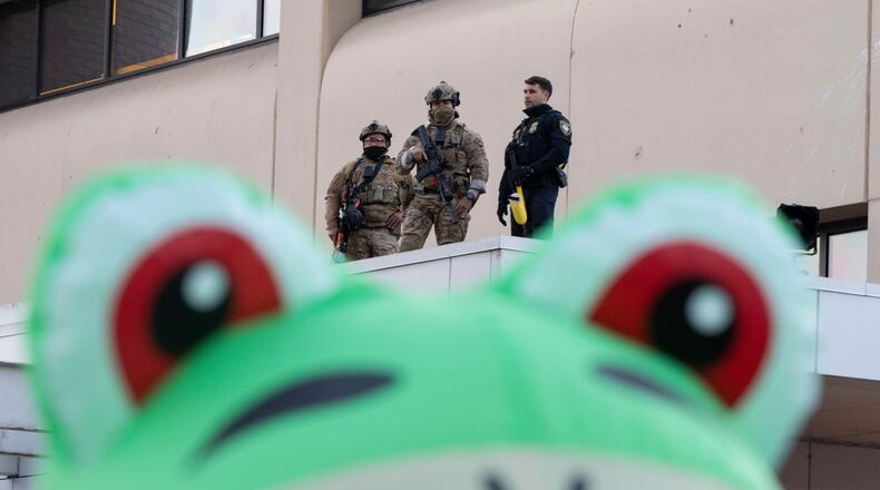 Law enforcement officers watch from a ledge of a United States Immigration and Customs Enforcement (ICE) facility as a protester stands outside in an inflatable frog costume on Tuesday, Oct. 21, 2025, in Portland, Ore. (AP Photo/Jenny Kane)