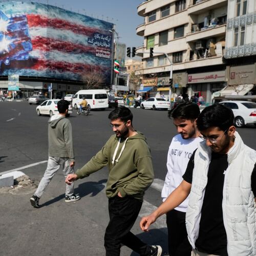 Pedestrians walk past a billboard depicting a U.S. aircraft carrier with damaged fighter jets on its deck and a sign in Farsi and English reading, "If you sow the wind, you'll reap the whirlwind," at Enqelab-e-Eslami (Islamic Revolution) Square in Tehran, Iran, Sunday, Feb. 22, 2026. (AP Photo/Vahid Salemi)