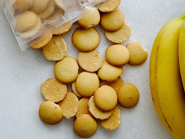 Vanilla wafers scattered beside a partially opened package of wafers with a ripe yellow banana along the right side.