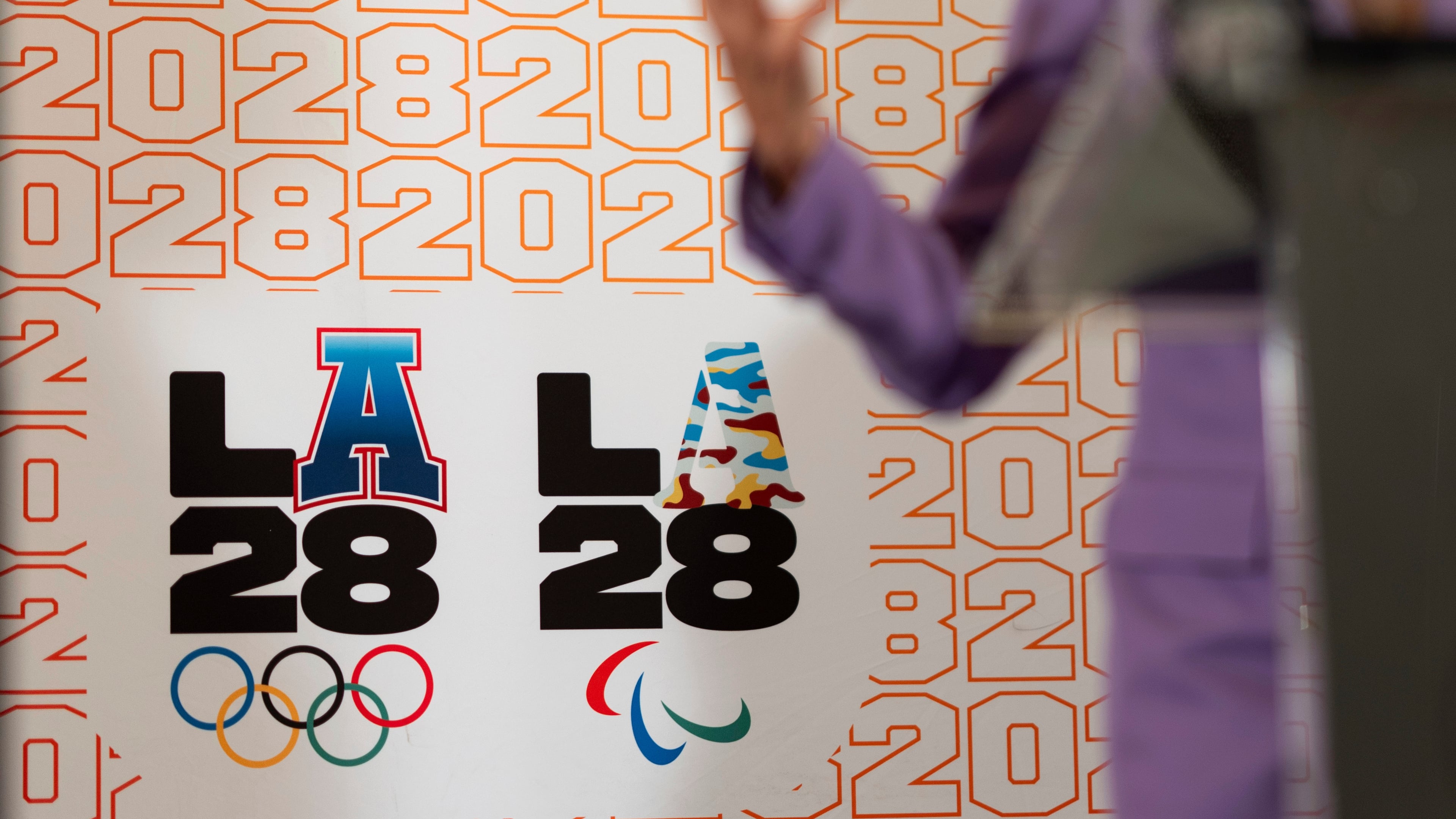 FILE - LA28 logos decorate a backdrop as First lady Jill Biden speaks at a reception at the U.S. Chief of Mission Residence to commemorate the opening of the 2024 Summer Olympics and celebrate the upcoming 2028 Olympic Games, to be held in Los Angeles, Saturday, July 27, 2024, in Paris. (AP Photo/David Goldman, File)
