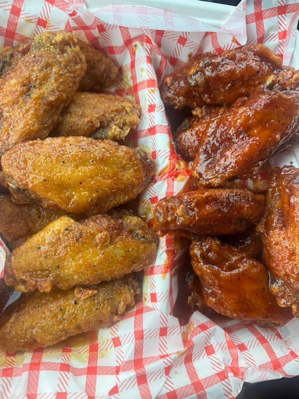 A half-and-half order of hot wings in a takeout box with a red-checked liner paper, the left wings with a pale dry rub and right wings with wet sauce