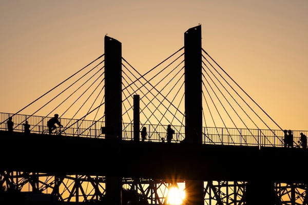 Poeple walk across the Big Four Bridge as the sun sets at Waterfront Park on Sunday, June 22, 2025, in Louisville, Ky. (AP Photo/Jon Cherry)