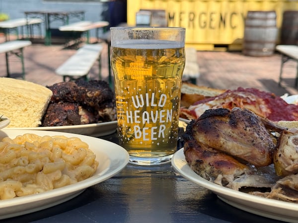 A glass of wild heaven beer sits on a picnic table surrounded by plates of food, including mac and cheese, jerk chicken and cornbread