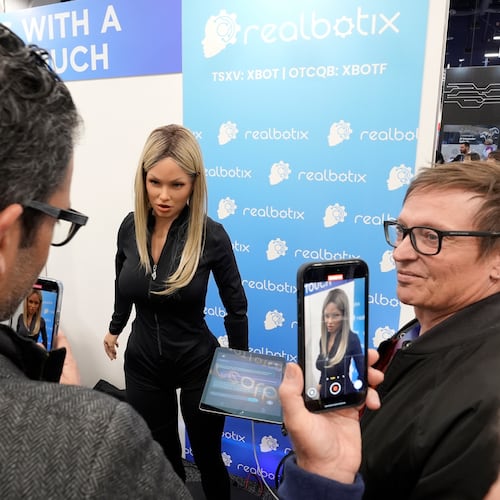 FILE - A Realbotix humanoid robot, center, speaks with attendees at a Realbotix booth during the CES tech show Jan. 8, 2025, in Las Vegas. (AP Photo/Abbie Parr, File)